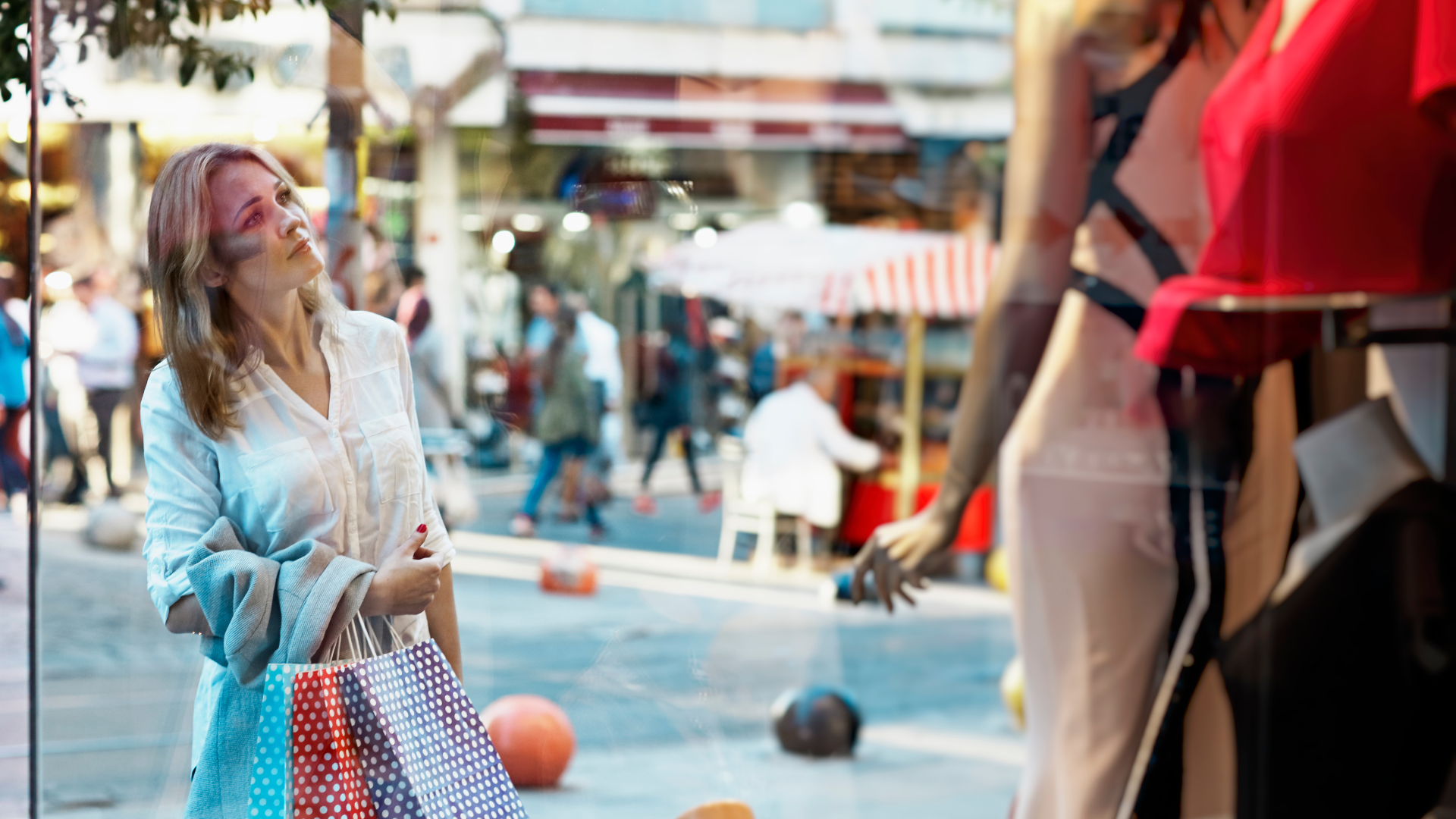 blonde woman looking through shop window at visual merchandising display 